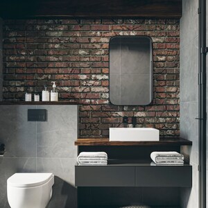 May include: A modern bathroom with a white porcelain toilet, a white porcelain sink, and a dark wood countertop. The walls are tiled with gray tiles and a brick wall. There is a large mirror above the sink.