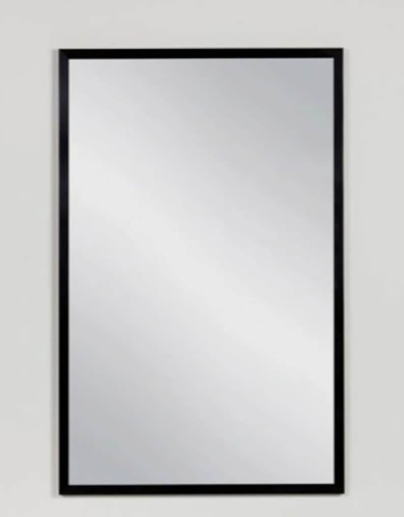 Puede incluir: Un espejo rectangular con marco negro y superficie reflectante.