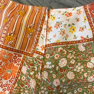 May include: A patchwork skirt with a back zip fastening. The skirt features a variety of floral patterns in shades of orange, brown, green, and white.