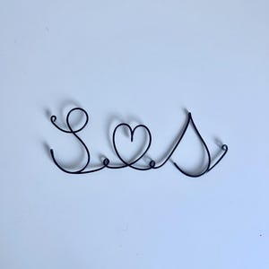 May include: A black wire sculpture of the word "Seas" with a heart in the middle.