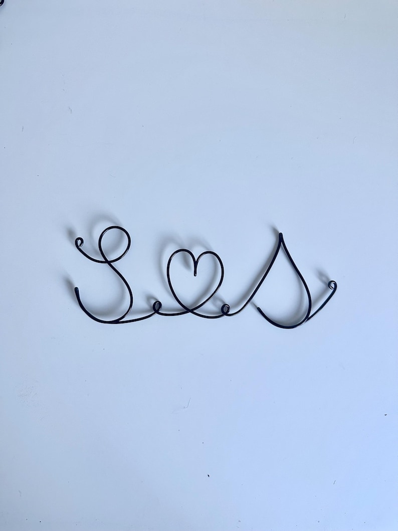 May include: A black wire sculpture of the word "Seas" with a heart in the middle.