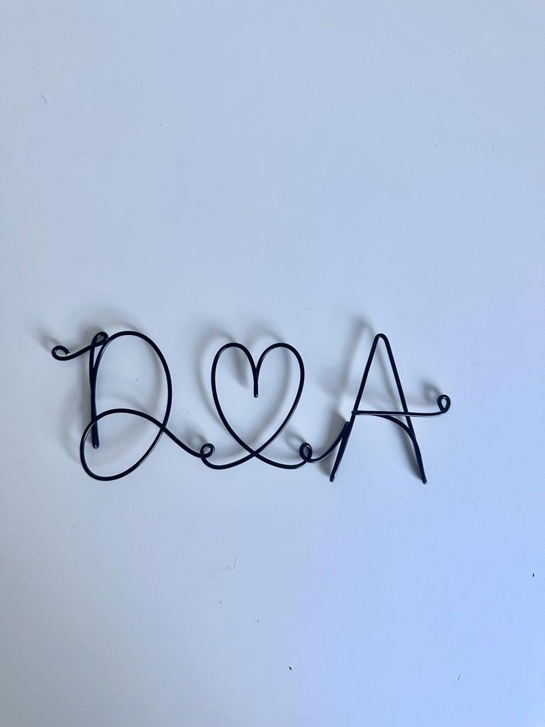 May include: A black wire sculpture of the letters "D & A" with a heart in between the letters.