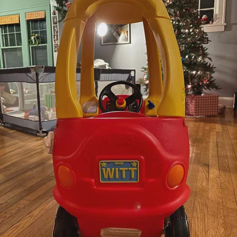 Puede incluir: Un coche de juguete de pl&aacute;stico rojo y amarillo con techo alto, volante negro y una matr&iacute;cula azul en la parte trasera que dice OHIO WITT. El veh&iacute;culo cuenta con dos luces traseras circulares de color naranja y ruedas de color negro.