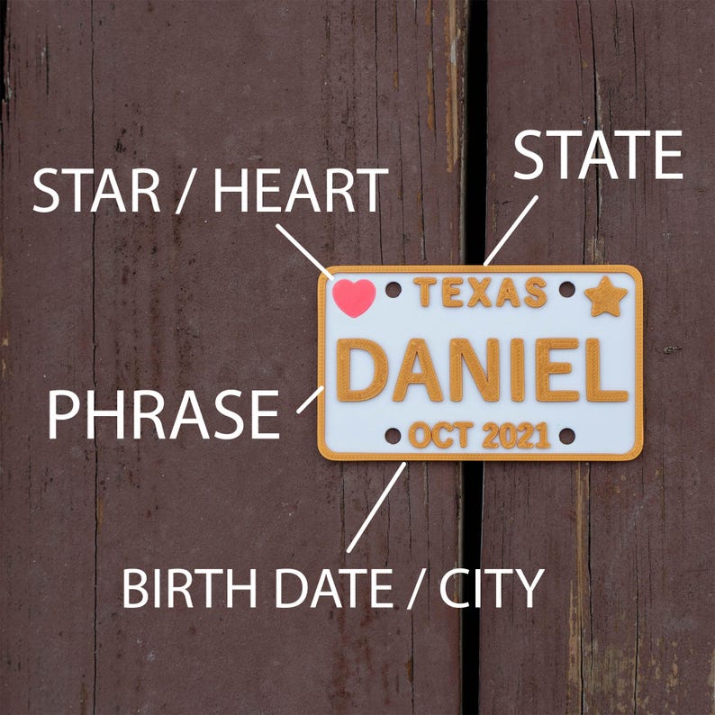 Puede incluir: Una placa de matr&iacute;cula rectangular blanca con borde dorado, que presenta el texto dorado TEXAS, DANIEL y OCT 2021. Incluye un icono de coraz&oacute;n rosa y una estrella dorada. L&iacute;neas blancas y etiquetas se&ntilde;alan estas caracter&iacute;sticas con las palabras STAR / HEART, STATE, PHRASE y BIRTH DATE / CITY.