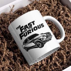 Może przedstawiać: Biały kubek ceramiczny z czarno-białym obrazkiem klasycznego samochodu i tekstem "The Fast and the Furious".