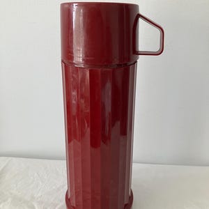 May include: A white ceramic mug with a black handle and the text "But First, Coffee" in a bold, black font. The mug is set against a neutral background, highlighting its simple design.