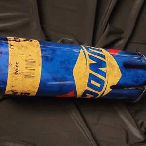 May include: A blue and yellow tumbler with the word "DON" in a diamond shape. The tumbler has a yellow band with the text "20 OZ" and a barcode. The tumbler is cylindrical and has a white rim.