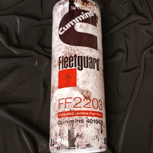 May include: A white, brown, and red metal tumbler with a distressed look. It features the Cummins logo, the words "Fleetguard" and "FF2203", and the text "Extended Service Fuel Filter Cummins 4010476".