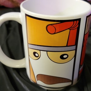 May include: White ceramic coffee mug with a cartoon illustration of a carton of milk with a red straw and a mustache. The carton has a yellow top and a gray lid. The mug has a black handle.