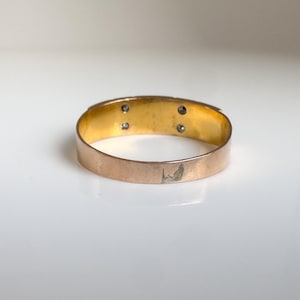 May include: A gold-toned ring with a rose gold exterior and a gold interior. The ring features four small, round, clear stones. The band shows some wear and tear. The ring is set against a white background.