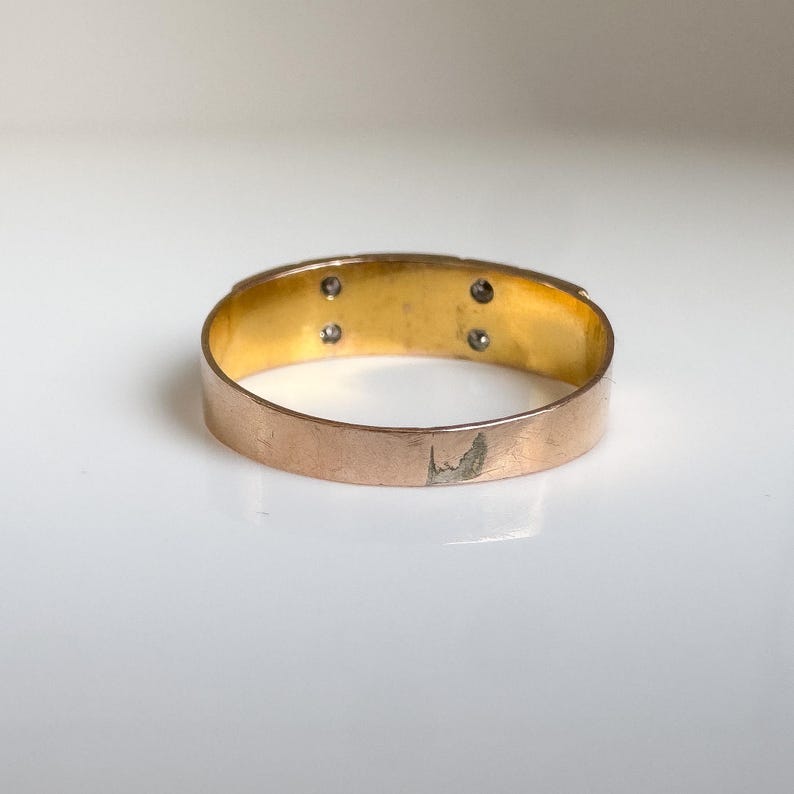 May include: A gold-toned ring with a rose gold exterior and a gold interior. The ring features four small, round, clear stones. The band shows some wear and tear. The ring is set against a white background.