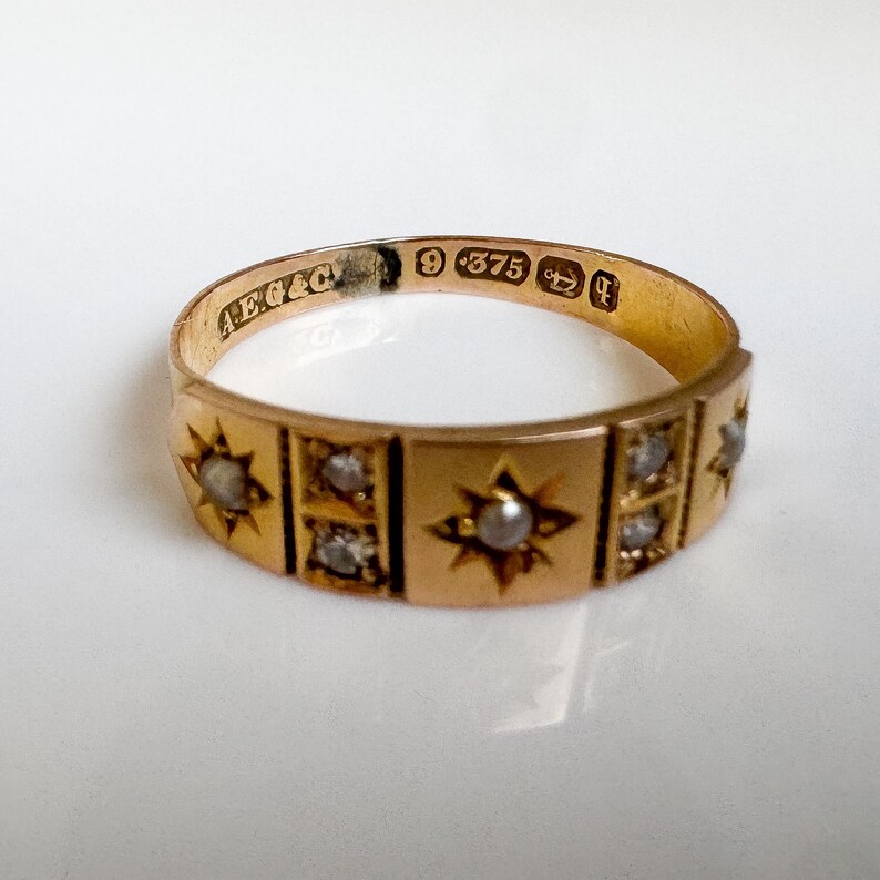 May include: A gold ring with star and square designs, set with small gemstones. The ring has a polished finish and is stamped with markings including "9 375". The ring is likely vintage or antique.