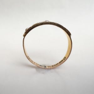 May include: A gold ring with a textured band and small, raised embellishments. The ring's interior is smooth and polished, reflecting the light. The ring appears to be a size 7.