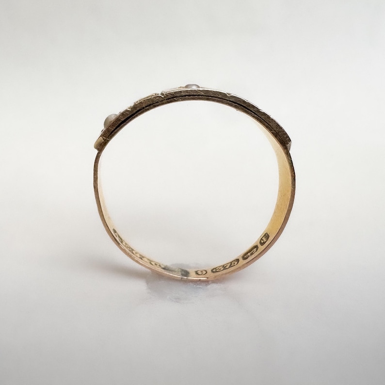 May include: A gold ring with a textured band and small, raised embellishments. The ring's interior is smooth and polished, reflecting the light. The ring appears to be a size 7.