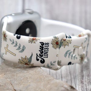 Puede incluir: Banda blanca para Apple Watch con un patrón floral y el texto "Jesus Loves Us".