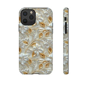 May include: A white and gold floral phone case with a 3D effect. The case features a pattern of white flowers with gold leaves and accents.