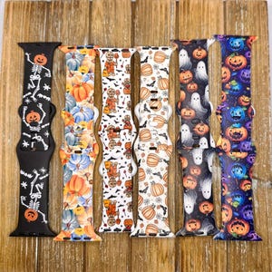 Könnte beinhalten: Sechs verschiedene Apple Watch-Armbänder mit Halloween-Motiven. Die Armbänder sind schwarz, weiß, blau und orange mit verschiedenen Mustern, darunter Kürbisse, Geister, Skelette und Fledermäuse.