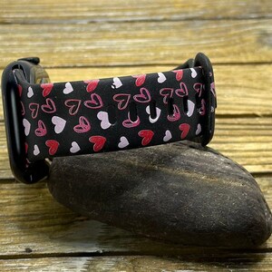 May include: Black watch band with a pink and white heart pattern.