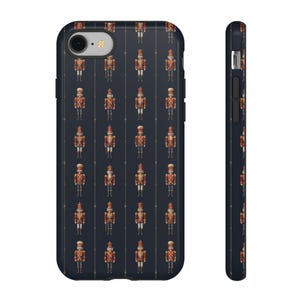 May include: A navy blue phone case featuring a repeating pattern of toy nutcracker soldiers in red, gold, and brown. The case has a glossy finish and a slim profile, with a camera cutout and side buttons.