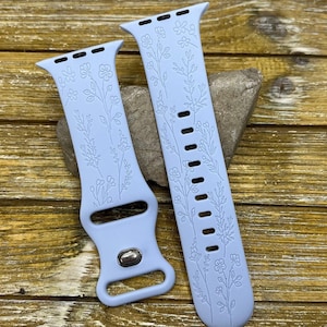 Peut inclure: Deux bracelets de montre bleu clair avec des motifs floraux. Les bracelets sont en matériau souple et présentent des motifs délicats de fleurs et de feuilles. Les bracelets sont présentés sur une surface en bois.