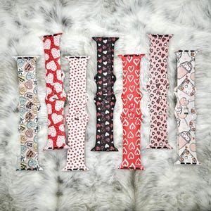 May include: Seven different Apple Watch bands with various heart-themed patterns. The bands are in red, pink, black, and white with small hearts printed on them.