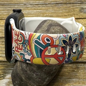 May include: A white Apple Watch band with a colorful psychedelic print featuring peace signs, flowers, and the word "Peace".