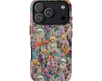 May include: A phone case featuring a colorful floral design with embroidered-style flowers and small skeleton figures. The case has a black camera module with three lenses and a flash.