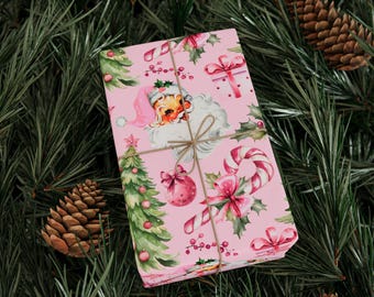 May include: A wrapped gift with a pink Christmas-themed pattern featuring Santa Claus, Christmas trees, candy canes, and bows. The gift is tied with twine and rests on a bed of green pine needles, with pine cones scattered around.