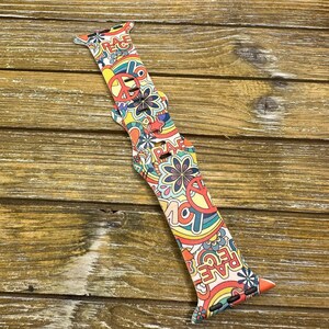May include: A colorful Apple Watch band with a psychedelic pattern featuring peace signs, flowers, and the word "Peace" repeated throughout.