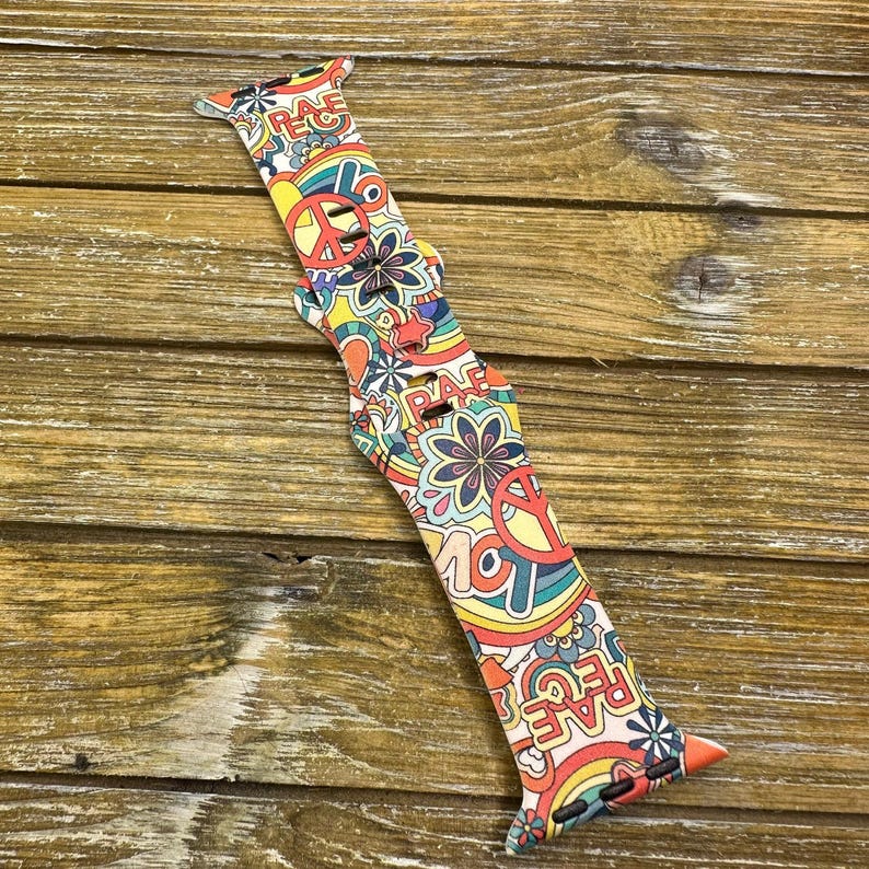 May include: A colorful Apple Watch band with a psychedelic pattern featuring peace signs, flowers, and the word "Peace" repeated throughout.
