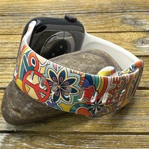 May include: White Apple Watch band with a colorful psychedelic pattern featuring peace signs, flowers, and rainbows. The band is made of silicone and has a smooth finish.