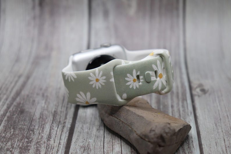 Puede incluir: Una correa de reloj de silicona verde y blanca con estampado de margaritas. La correa est&aacute; dise&ntilde;ada para Apple Watch.
