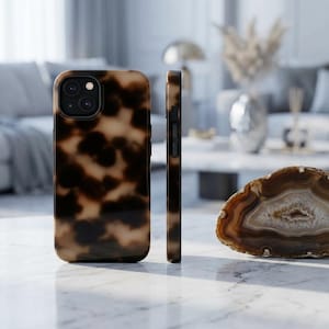 May include: A tortoiseshell-patterned phone case, displayed from multiple angles. The case has a glossy finish with a dark brown and tan pattern. The phone case is shown next to a decorative agate stone.