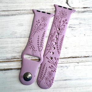 May include: Two lilac purple silicone Apple Watch bands with a floral design. The bands have a raised floral pattern and are designed for the Apple Watch.
