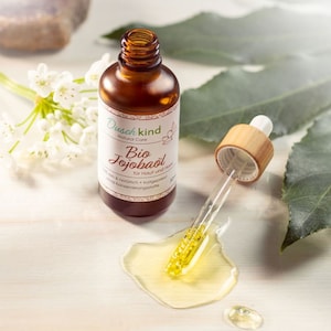 Op de afbeelding: Een bruine glazen fles met een druppelaar gevuld met een heldere gele vloeistof. De fles is gelabeld "Dusch kind Natural Care Bio Jojobaöl für Haut und Haar 100% rein & natürlich - kaltgepresst ohne Konservierungsstoffe".