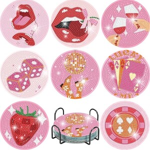 May include: Set of nine pink coasters with various designs, including red lips, dice, playing cards, a strawberry, and a disco ball. The coasters are round and have a textured appearance. A black metal stand holds the coasters.