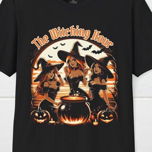 以下が含まれることがあります： 黒いTシャツ。3人の魔女、カボチャ、コウモリのグラフィックが特徴で、「The Witching Hour」の文字が入っています。デザインはオレンジと白です。Tシャツは柔らかい素材で作られています。ハロウィーンをテーマにしています。