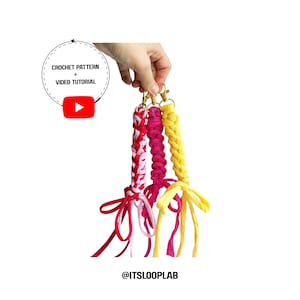 Op de afbeelding: Drie gevlochten stoffen sleutelhangers in roze, magenta en geel, elk bevestigd aan een goudkleurige metalen draaisluiting. De tekst CROCHET PATTERN + VIDEO TUTORIAL is zichtbaar in een cirkelvormig kader en onderaan staat @ITSLOOPLAB.