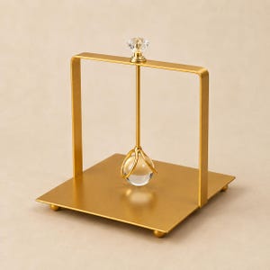 Peut inclure: Un porte-serviettes en métal doré doté d'une base carrée avec quatre petits pieds sphériques. Une poignée arquée s'élève de la base, surmontée d'un embout en cristal transparent à facettes. Une tige centrale maintient une sphère en verre.