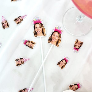 K&ouml;nnte beinhalten: Wei&szlig;e Cocktailr&uuml;hrer mit dem Gesicht einer l&auml;chelnden Frau und dem Schriftzug "Happy Birthday" auf einem rosa Kr&ouml;nchen. &Auml;hnliche Bilder der Frau mit Partyhut sind verstreut. Ein Glas mit einem rosa Getr&auml;nk ist zu sehen.
