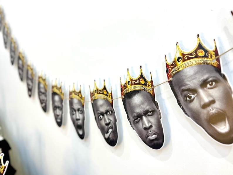 May include: A string of paper cutouts of a person's face wearing a gold crown. The faces have various expressions, including open mouths and sticking out tongues. The crowns are gold with red and black accents.