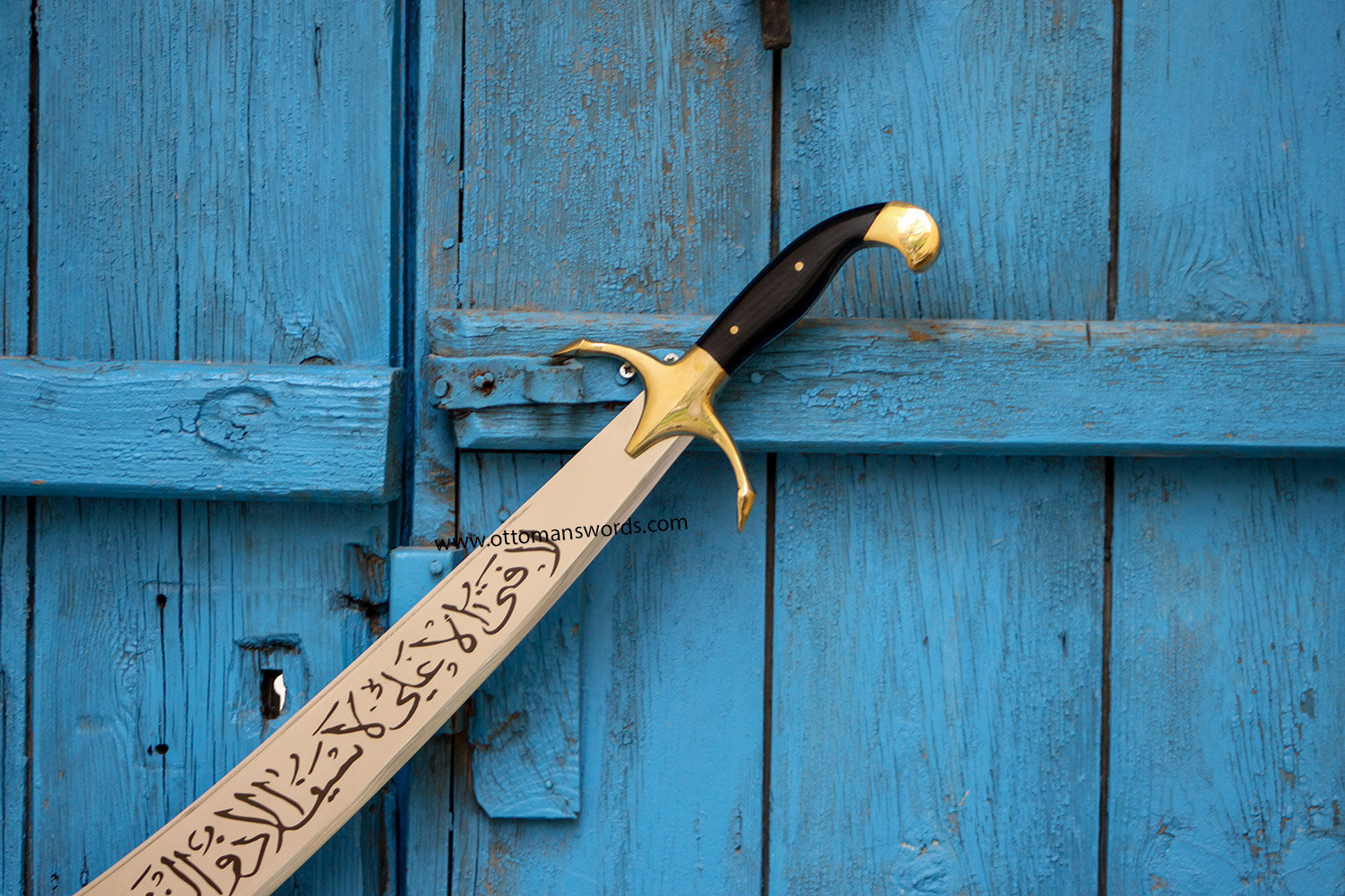  An image of an Islamic sword from the 10th century with a curved blade and a gold hilt, resting on a blue wooden door.