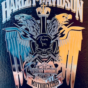 Könnte beinhalten: Ein silbernes Harley-Davidson Motorrad-Emblem mit Totenkopf und Knochen, zwei Adlern und den Worten "Motor", "Harley Davidson", "Cycles" und "Motorcycles".