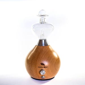 May include: An essential oil diffuser with a wooden base and a clear glass top. The wooden base has a rounded shape and features the text "Amrita Court". The diffuser has a silver-coloured base, a knob and a small button on the front.