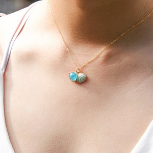 May include: A gold chain necklace with a blue and white seashell pendant. The seashell is open and has a small blue gem inside.