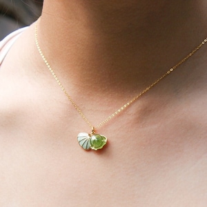 Può includere: Una collana con catena dorata con un ciondolo a forma di conchiglia verde e bianca.