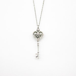 May include: A silver key necklace with a heart-shaped keyhole. The key is detailed with intricate scrollwork.