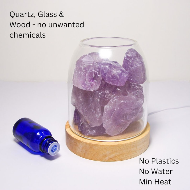 K&ouml;nnte beinhalten: Ein Glasdiffusor mit Holzsockel und Amethystkristallen im Inneren. Der Diffusor ist beleuchtet und hat eine blaue &auml;therische &Ouml;l-Flasche daneben. Der Text "Quartz, Glass & Wood - no unwanted chemicals" befindet sich oben im Bild. Der Text "No Plastics No Water Min Heat" befindet sich unten im Bild.