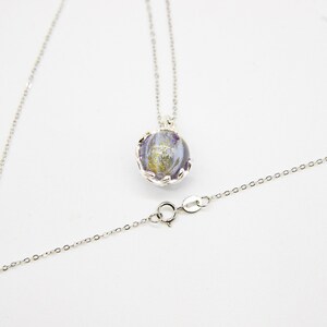 Op de afbeelding: Een zilveren ketting met een ronde hanger met een paars en gouden swirl-ontwerp.
