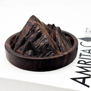 May include: A dark brown wooden mountain sculpture with a detailed, textured surface. The sculpture is placed in a round, dark brown wooden bowl.